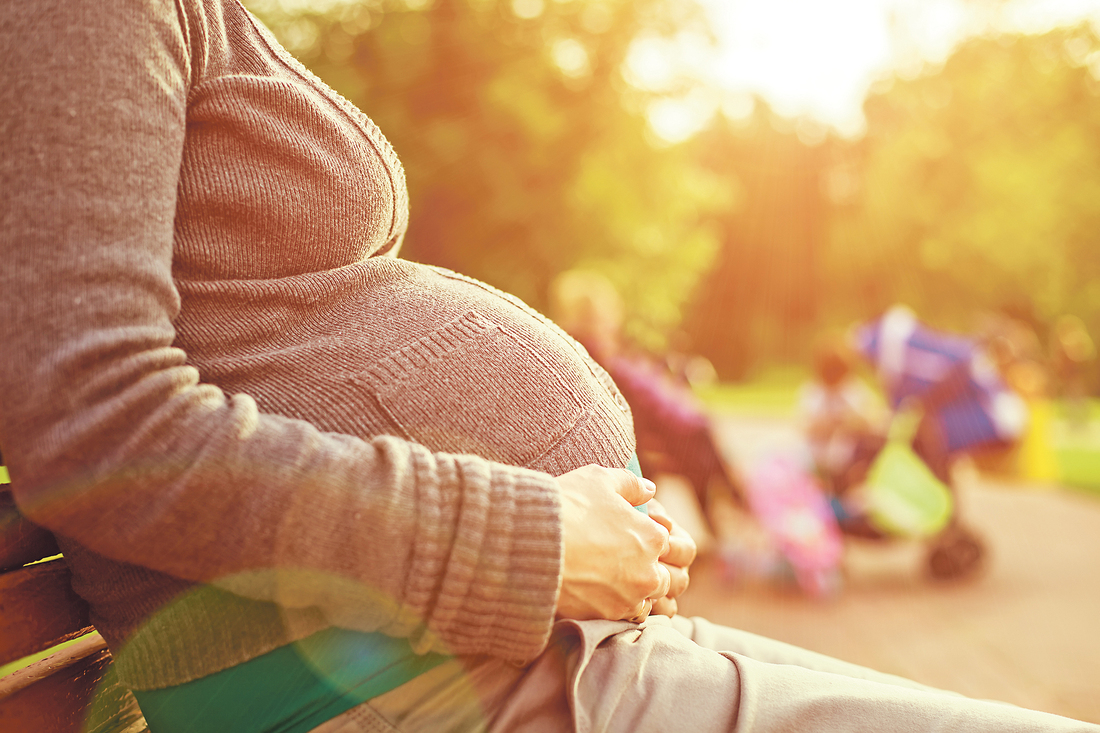 Pregnant woman sitting on a bench. on background the children play. warm weather