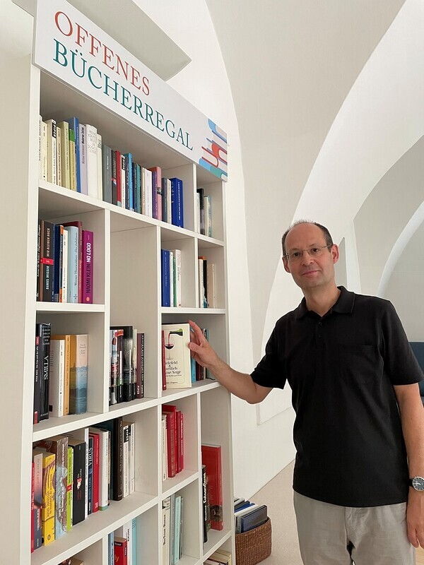 Günther Jäger lädt ein, das offene Bücherregal in der KHG zu nützen.