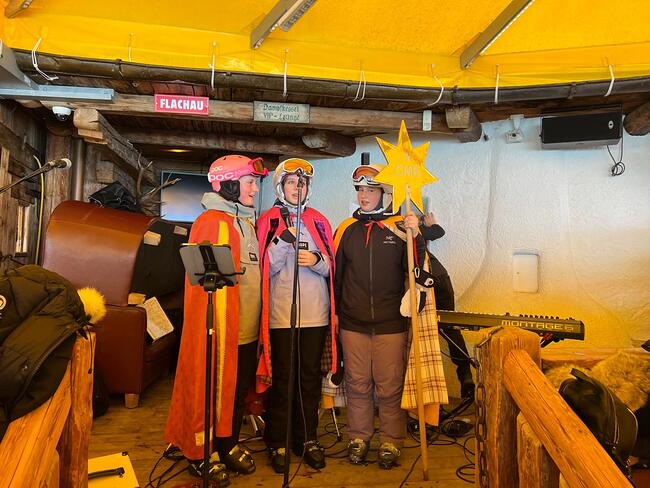 reudig erwartet: Die Heiligen Drei Könige mit Skihelm statt Krone singen auf der Bühne der Almhütten für den guten Zweck.